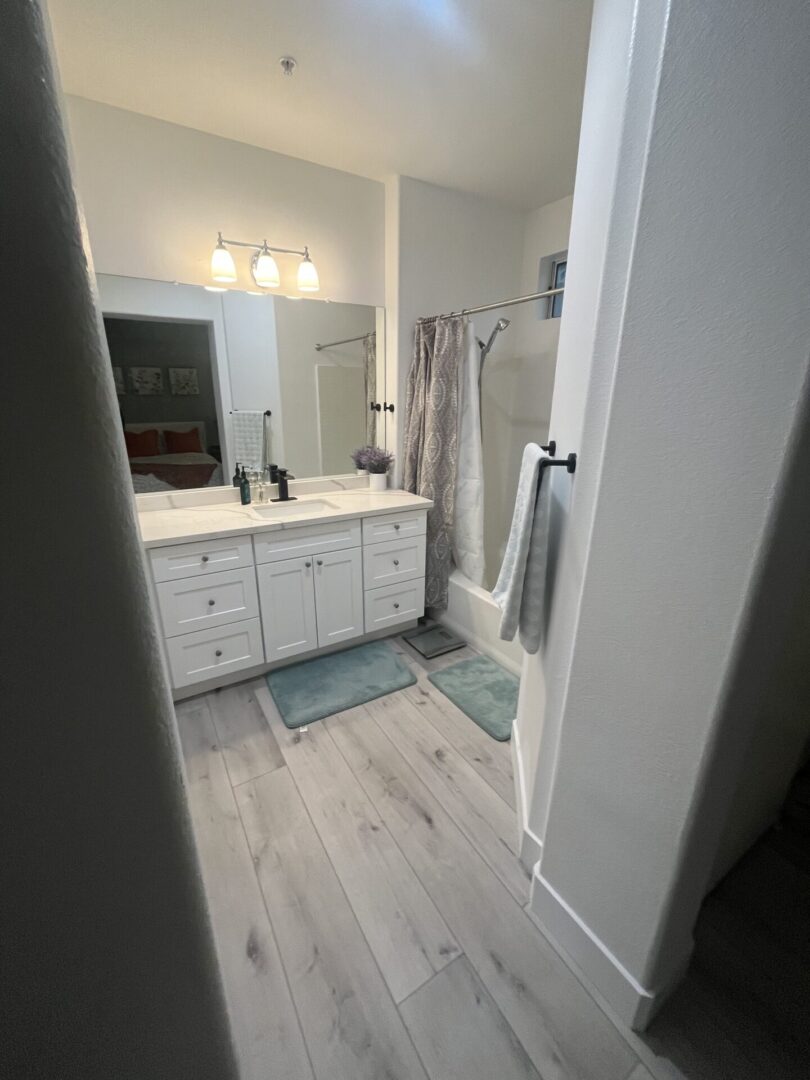 A bathroom with white cabinets and wood floors.
