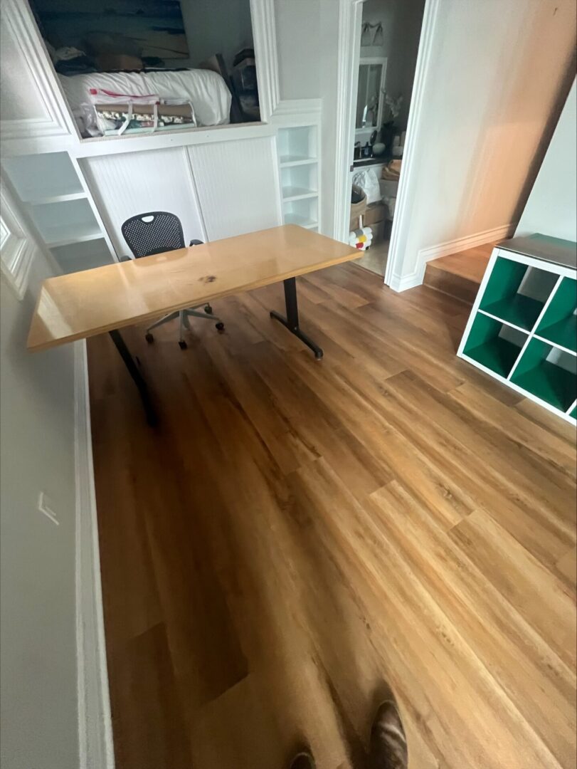 A wooden floor with a desk and shelves in the corner.